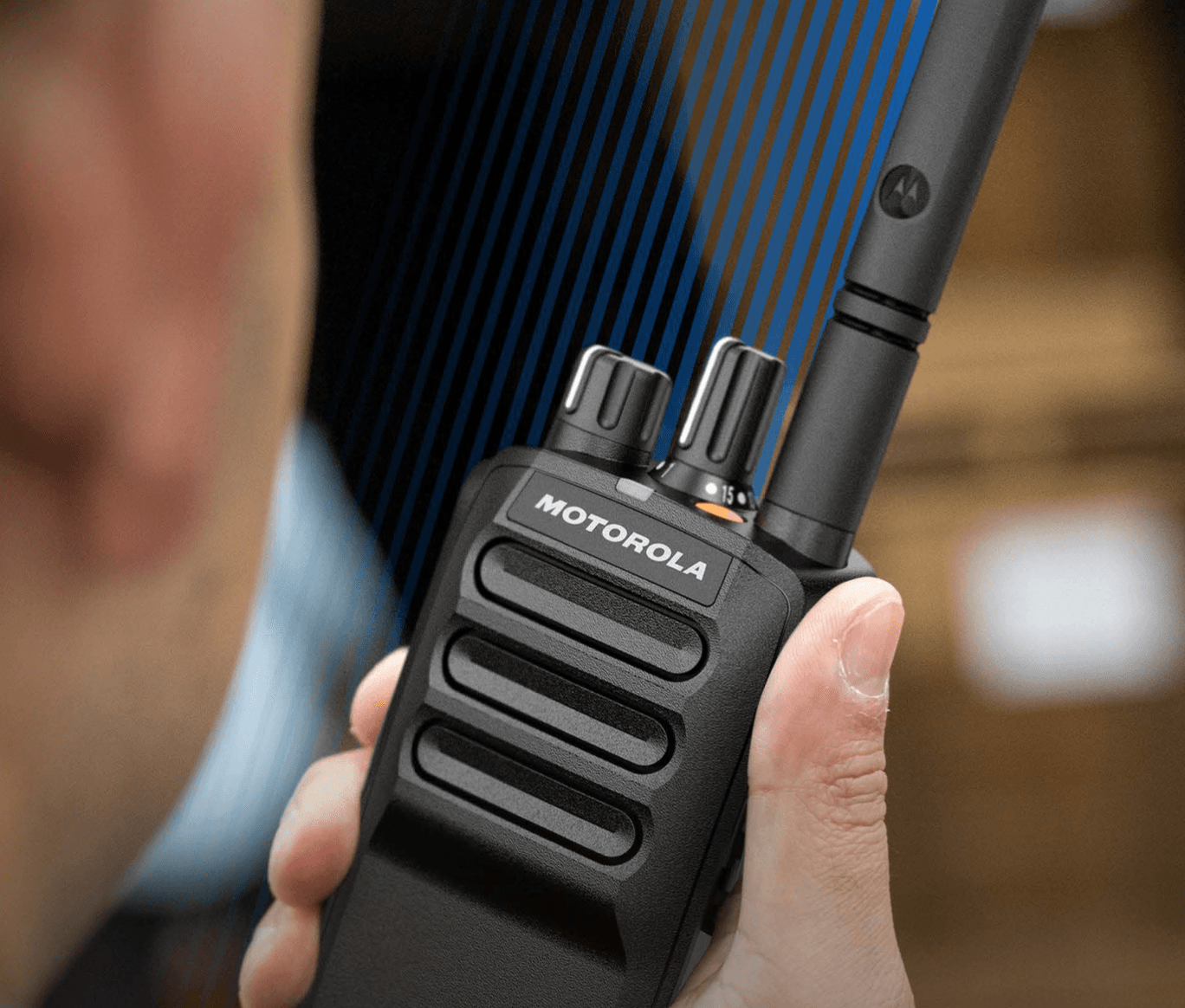 Mano sosteniendo un radioteléfono Motorola negro con líneas azules de señal sobre un fondo desenfocado.