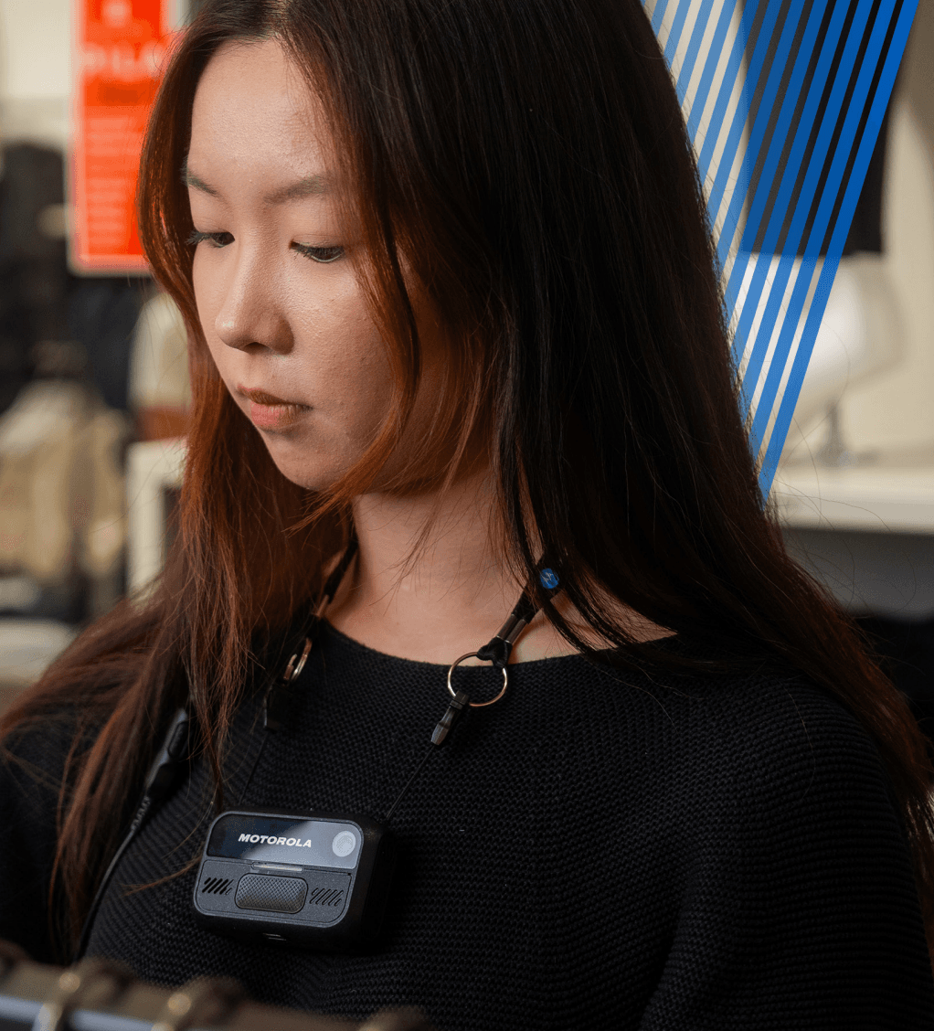 Mujer con suéter negro usando una cámara corporal Motorola sujeta a un cordón al cuello.